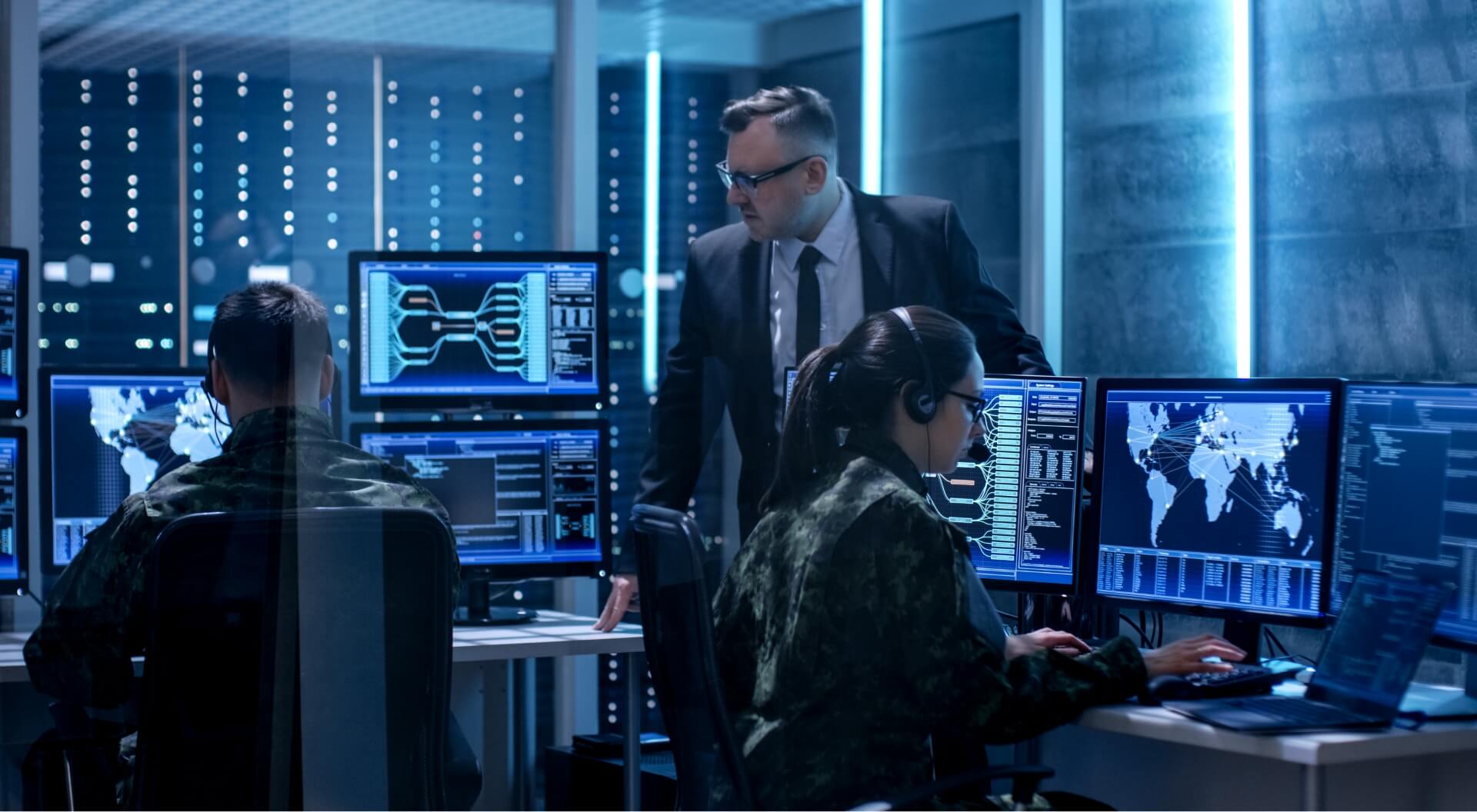 military personnel working on computers while a person in a suit oversees things in a command center environment