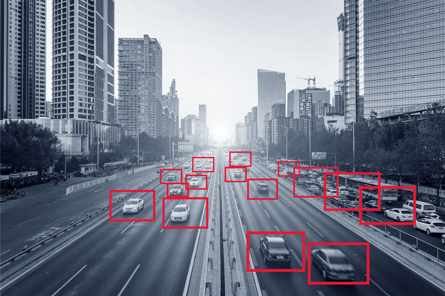 Overhead view of vehicles moving on roadways in an urban environment highlighted by red squares